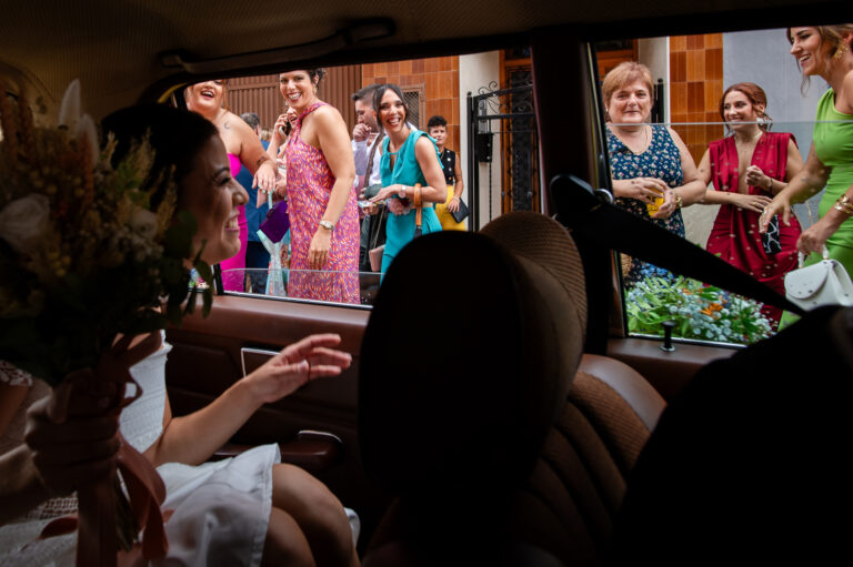 Fotografía de bodas documental: qué es | Adolf Boluda 8 Novia saludando contenta a sus amigas desde el coche de camino a la boda, reportaje documental en el Molí Canyisser, La Safor