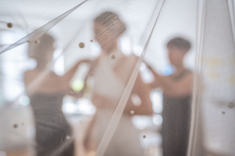 Fotógrafo de bodas natural y sin posados | Adolf Boluda 3 Detalle artístico del velo bordado con perlas de la novia; se intuyen las siluetas de su madre y su amiga, preparativos de boda en Alemania.