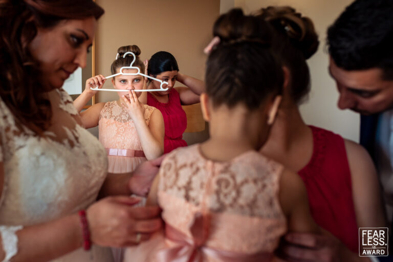 Fotógrafo de bodas natural y sin posados | Adolf Boluda 5 Una hija de la novia juega con una percha mientras su madre y su tío visten a las hermanas, boda en Mallorca. Foto premiada con un Fearless Award.