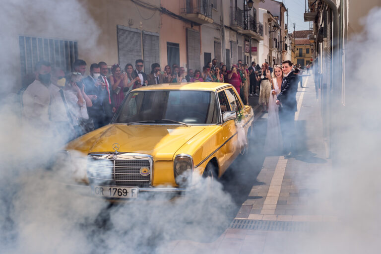 Fotógrafo de bodas natural y sin posados | Adolf Boluda 6 La novia sale de su casa en Bellreguard (Valencia) con su hermano, recibida entre el humo de una traca y un Mercedes amarillo clásico.