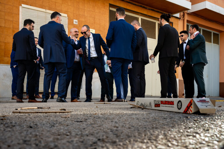 Fotografía de bodas documental: qué es | Adolf Boluda 2 Amigos saludando al novio junto a la caja y los restos de una traca recién tirada, boda documental en Bellreguard, La Safor
